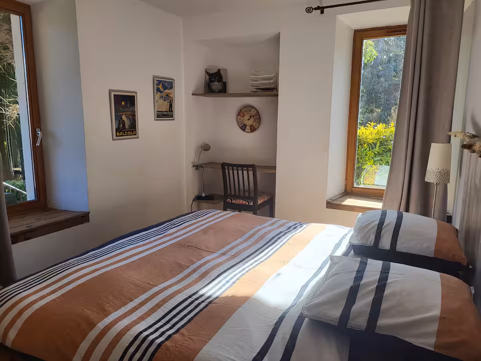 La chambre lumineuse et son grand lit, avec les fenêtres ouvertes sur la verdure